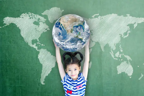 Photo of Happy Asian girl child student raising globe on school chalkboard for world literacy and gender equality concept. Elements of this image furnished by NASA