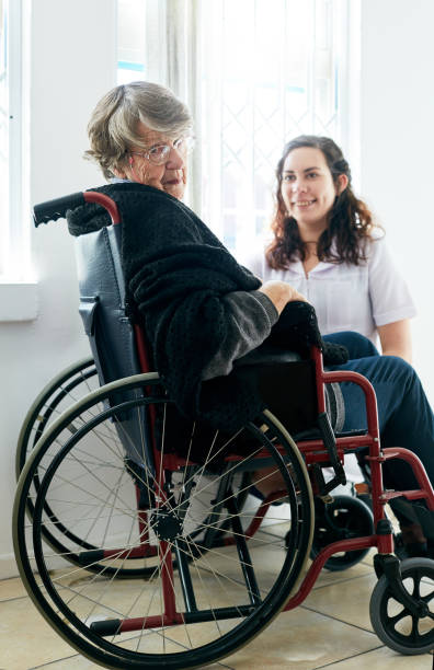 vieille femme au fauteuil roulant regarde autour de son soignant amical - women cheerful vertical 20s photos et images de collection