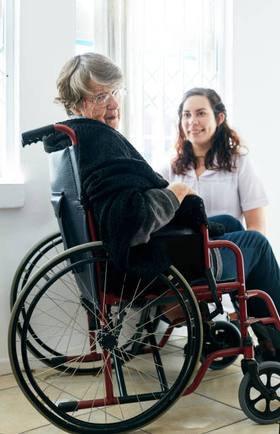 old woman in wheelchair looks round from her friendly caregiver - women cheerful vertical 20s imagens e fotografias de stock