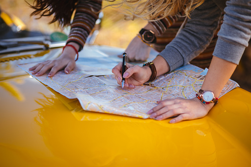 Close-up of women with retro car reading road map and making decisions about route