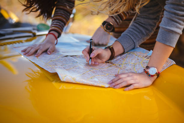 Women on summer road trip reading map for directions Close-up of women with retro car reading road map and making decisions about route land planning stock pictures, royalty-free photos & images