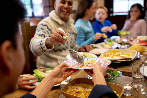 Serving Dinner to his Son A teenage boy holds out his plate for his father who serves him dinner at the dining table in a log cabin. food recall stock pictures, royalty-free photos & images