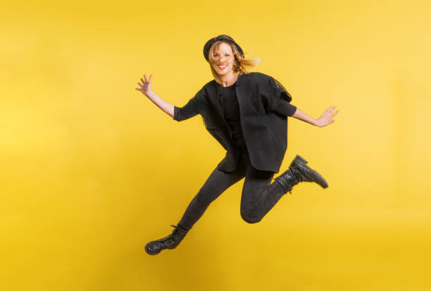 istock Young beautiful woman with black hat in studio on a yellow background, jumping. 964828448