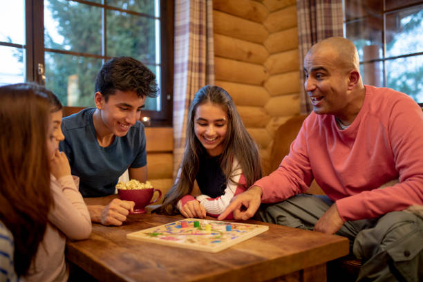 Playing a Board Game A family play a board game together in a log cabin. A mid adult man smiles and points at the game whilst talking to his daughter. board game stock pictures, royalty-free photos & images