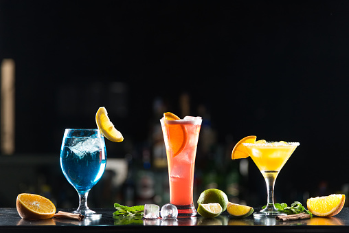 Multi-colored alcoholic cocktails with citrus in glasses of different shapes on the bar. Photo.