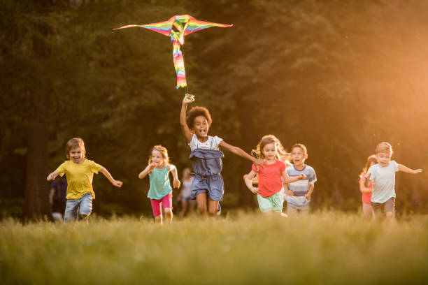 istock Large group of joyful kids running with a kite in springtime. 964835568