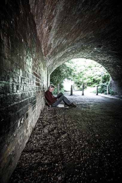 hombre senior sin hogar durmiendo áspero en túnel subterráneo oscuro - brick wall homelessness wall begging fotografías e imágenes de stock