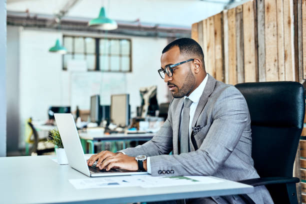 Catching up on some work emails Shot of a young businessman working on a laptop in an office stubble male african ethnicity facial hair stock pictures, royalty-free photos & images