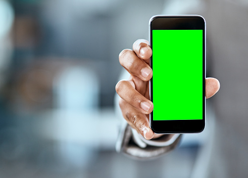 Closeup shot of an unrecognizable businessman holding up a cellphone with a green screen in an office