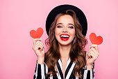 Charming pretty nice, comic, funny, modern, cheerful, laughing girl in black and white jacket having two small paper heart in hands, isolated on pink background