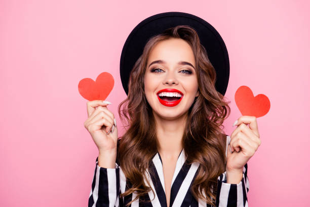 Charming pretty nice, comic, funny, modern, cheerful, laughing girl in black and white jacket having two small paper heart in hands, isolated on pink background Charming pretty nice, comic, funny, modern, cheerful, laughing girl in black and white jacket having two small paper heart in hands, isolated on pink background human lips photos stock pictures, royalty-free photos & images