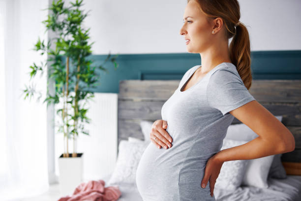 junge schwangere leidet unter rückenschmerzen - window human pregnancy home interior women stock-fotos und bilder