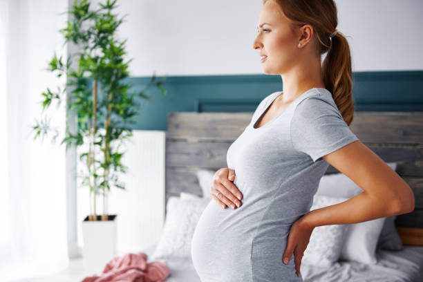 młoda kobieta w ciąży cierpi na ból pleców - window human pregnancy home interior women zdjęcia i obrazy z banku zdjęć