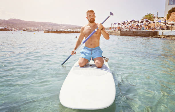 Adult bearded man beginner surfer kneel on paddle board on sea. Summer active vacation and water sport concept