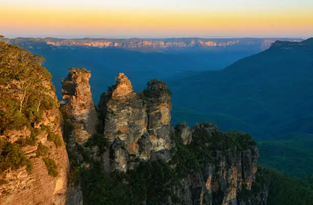 The last golden rays of the sun touching the tallest peaks of the Three Sisters rock formation before sunset in the Jamison Valley, part of the Blue Mountains in New South Wales, Australia.