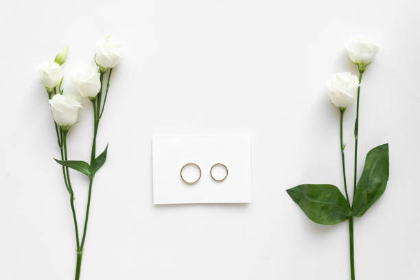 istock Wedding card with wedding rings and roses, on white marble . Top view. 964858334