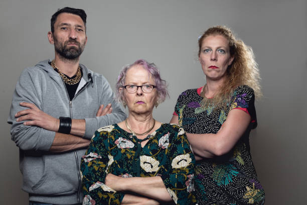 gangster trio: mother, adult son and his fiancée midadult couple and senior woman, standing with folded arms, looking into camera with serious expression it could be read as threatening as well, , the man is wearing golden necklaces and grey hoodie, the women very colorful clothes with many patterns, gang photos stock pictures, royalty-free photos & images