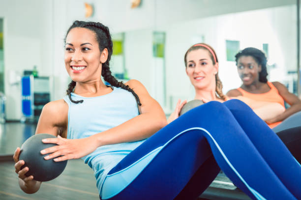 Beautiful woman exercising Russian twist with med ball for strong abs at the gym Beautiful young woman exercising Russian twist with med ball from sitting position for strong abs during group workout class for women at the gym the twist stock pictures, royalty-free photos & images