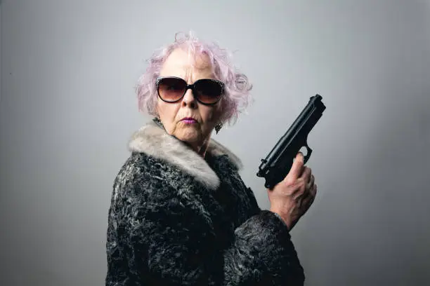 Senior woman, wearing fur coat and sunglasses, holding gun in her hand,  she has pink curly hair