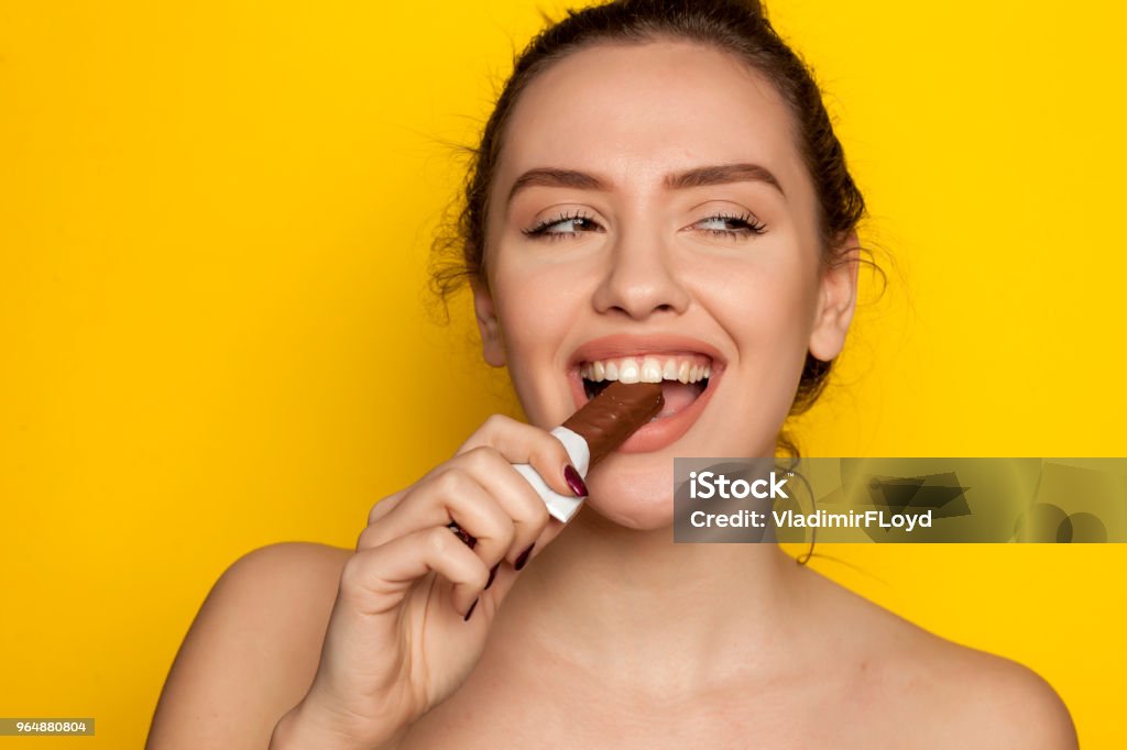 jeune femme heureuse profitant de manger du chocolat sur un fond jaune - Photo de Chocolat libre de droits
