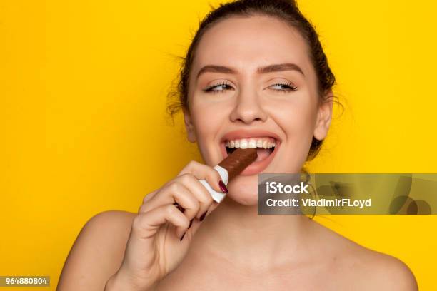 Young Happy Woman Enjoying Eating Chocolate On A Yellow Background Stock Photo - Download Image Now