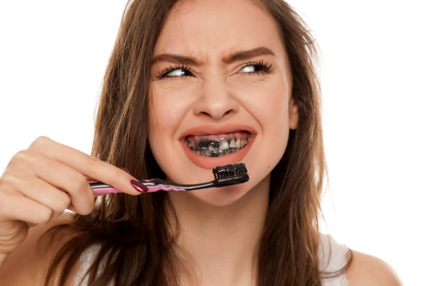 mujer joven cepillarse los dientes con una pasta de diente negro con cepillo de dientes activos de carbón y negro sobre fondo blanco - floyd fotografías e imágenes de stock