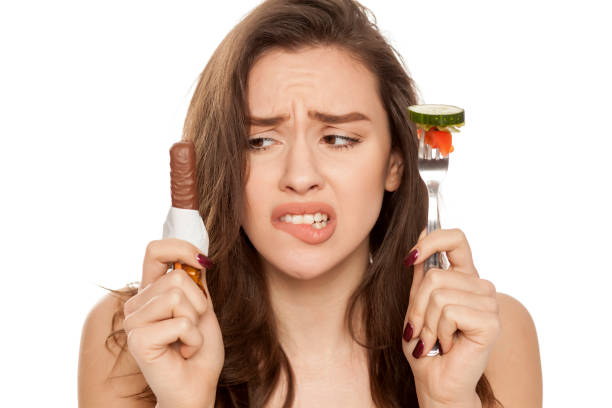 istock a young beautiful woman is tempted by chocolate and vegetable on white background 964883500