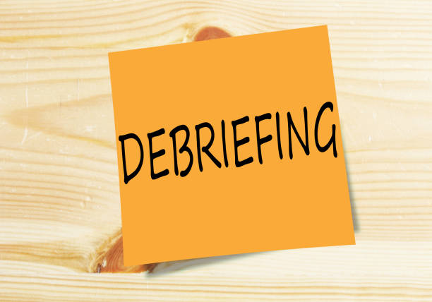 DEBRIEFING handwritten on orange small paper on wood texture background
