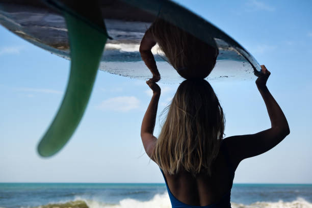 istock Young woman with surfboard walk on black sand beach 964887996