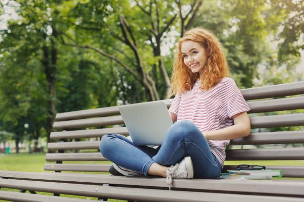 istock Happy woman is using laptop in the park 964890470