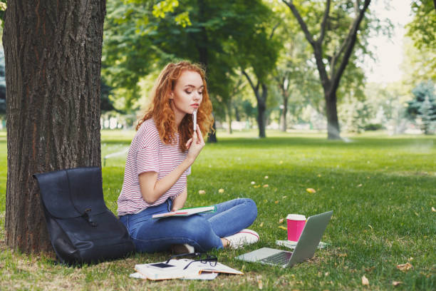 istock Young woman sitting with notebook on grass 964890570