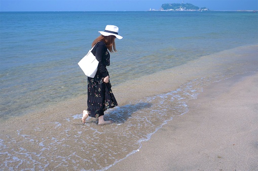 Girl in bikini sitting on the sand with cap on her head watching sea
