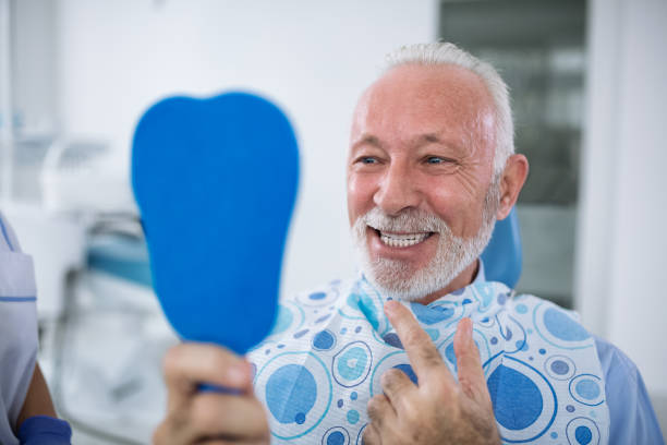 Smiling and satisfied patient after treatment Smiling and satisfied patient after treatment looks at teeth in mirror Best Smileat dental clinic stock pictures, royalty-free photos  images