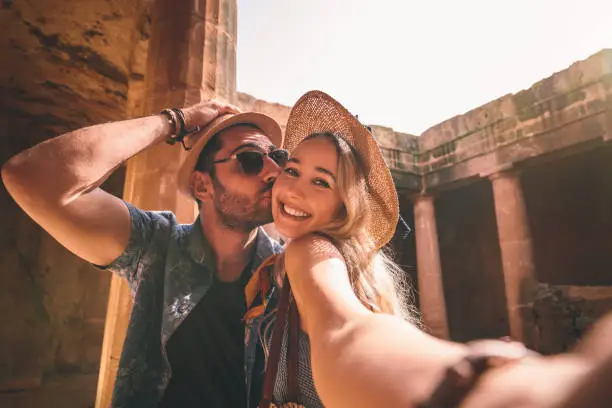 Tourists couple taking selfies while doing sightseeing at ancient monument with stone columns in Europe