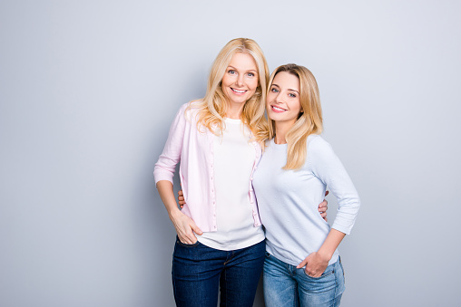 Portrait of attractive charming pretty cute similar mother and daughter embracing holding hands in pocket of pants standing over grey background