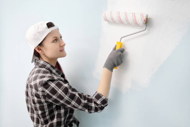 istock Girl painter, designer and worker paints a roller and brush the wall. Smiling, working with pleasure, close-up 964903392