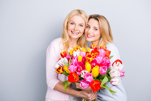 Portrait of charming pretty attractive mother and daughter having big bouquet of colorful aromatic tulips looking at camera bonding isolated on grey background