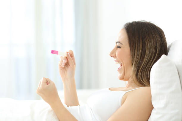 excited woman checking a positive pregnancy test in the bed - artificial insemination imagens e fotografias de stock