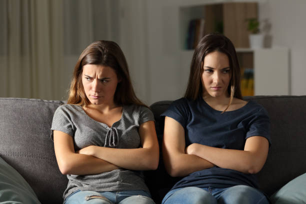 Angry friends ignoring each other at home in the night Front view portrait of two angry friends ignoring each other at home in the night sitting on a couch in the living room at home sister stock pictures, royalty-free photos & images