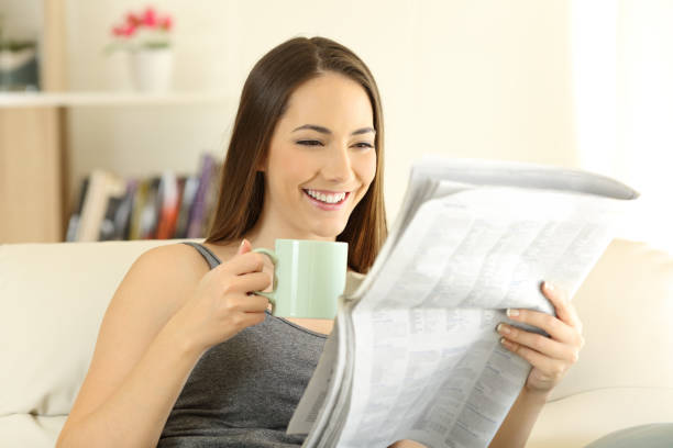 istock Happy female reading a newspaper on a couch 964916136