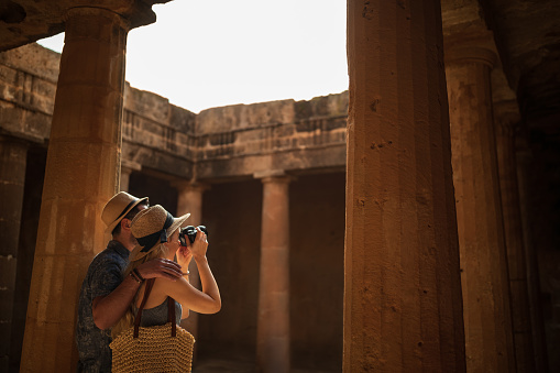 Young tourists couple in Greece taking photos of ancient classical architecture stone columns archaeological site