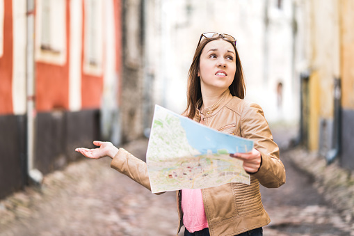 Woman lost in the city. Confused traveler holding map and spreading hands in old town. Disappointed and worried tourist having problem. Frustrated and unhappy during vacation. Wrong way or dead end.