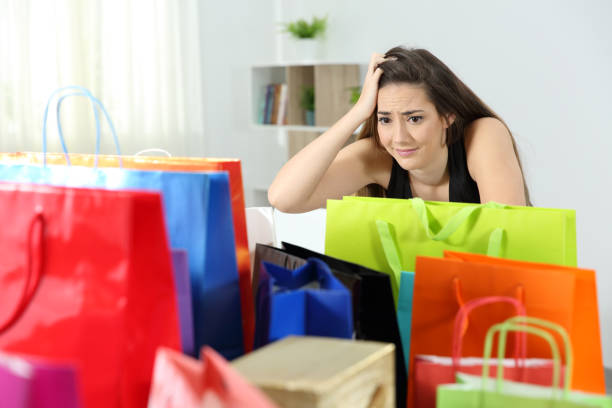 Worried shopaholic woman after multiple purchases Worried shopaholic woman after multiple purchases in colorful shopping bags at home excess stock pictures, royalty-free photos & images