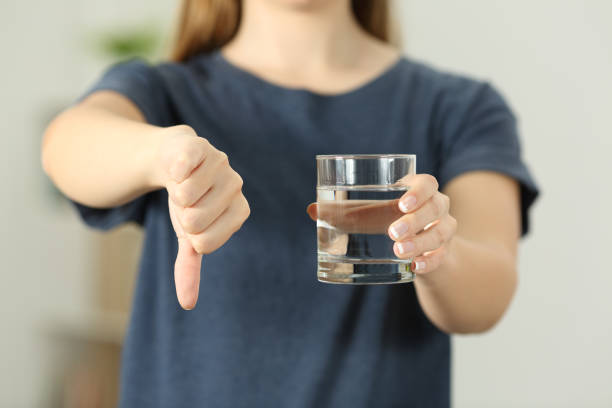 mujer que sostiene un vaso de agua con los pulgares hacia abajo - infame fotografías e imágenes de stock