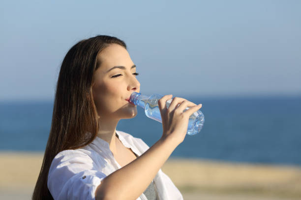 istock Lady drinking water from a bottle on the beach 964929144