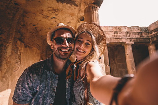 Smiling tourists on summer vacations in Greece taking selfies at ancient landmark with stone columns