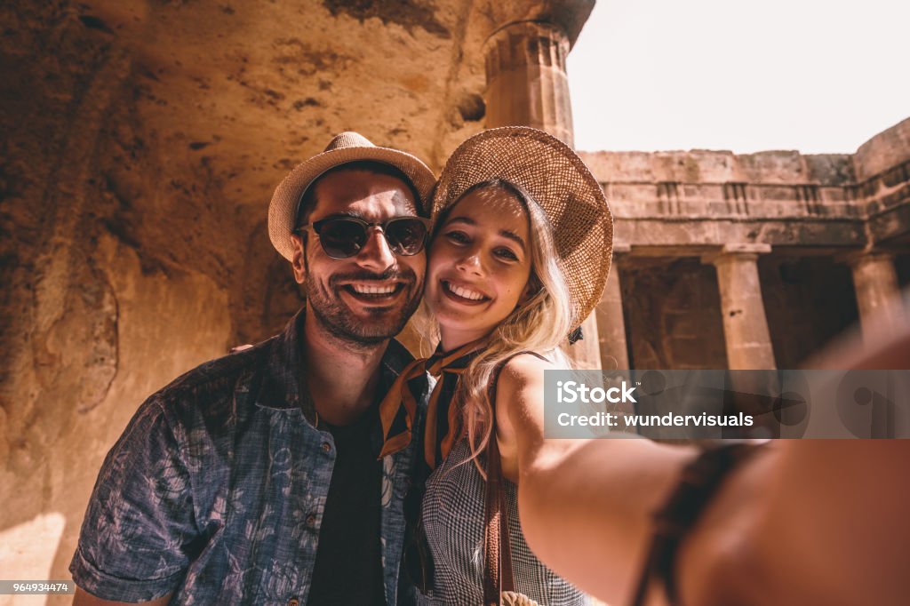 Young tourists couple taking selfies at ancient monument in Italy Smiling tourists on summer vacations in Greece taking selfies at ancient landmark with stone columns Travel Stock Photo