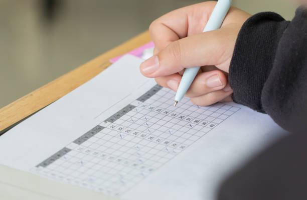 istock Education test concept : Hands with pen over application form, Students taking exams, writing examination room with undergraduate inside. Student sitting learning lessons doing final in classroom 964938208