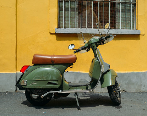 Milan, Italy - May 27, 2018: Green Piaggio Vespa LML T5 150 parked on side of street with yellow background