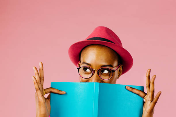 the reader: portrait of a happy young woman full of joy holding a book - woman with glasses reading a book imagens e fotografias de stock